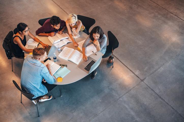 Group of students studying on a laptop at a round table with open books