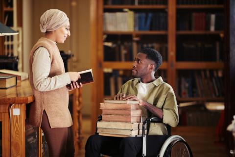 Student in a wheelchair talking to a friend in the library