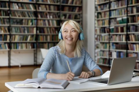 Girl sitting in library with books and laptop, smiling